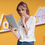 Vrouw met tablet voor een evenwichtsbalk waarop een huis en procentteken uit balans staan