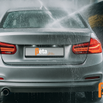 Zilverkleurige auto wordt gewassen in een automatische wasstraat met waterstralen en borstels – illustratie bij schade en verzekeringstips van Bèta Financiële Diensten